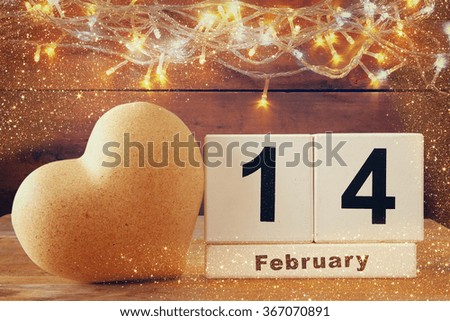 February 14th wooden vintage calendar next to heart on wooden table. vintage filtered 