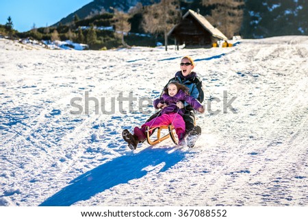 Mother and little child are sledging very fast in ski mountain resort. High speed braking. Active family vacation on snow in the nature.