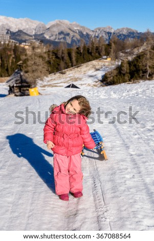 Girl is pulling snow sledge in ski resort  wearing winter clothes. High mountain ski resort, vacation, holiday and sunny day mountain peaks.