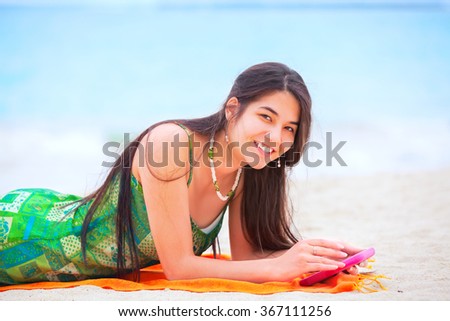 Beautiful biracial teen girl lying on tropical beach using cell phone