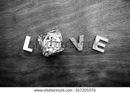word love made up of colorful wooden letters with dirty ashtray full of butts instead of letter O on a wooden board. February 14, Valentine's Day. Black and white.