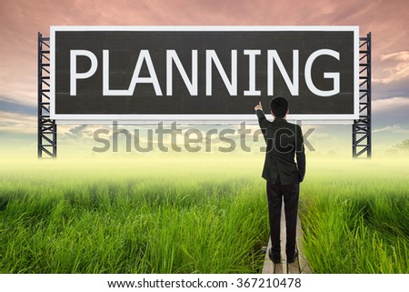 business man standing on wood bridge between rice field and pointing with large sign of planning (business concept)