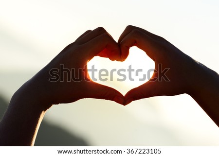 Hands forming a heart shape at sunset with mountains background.
