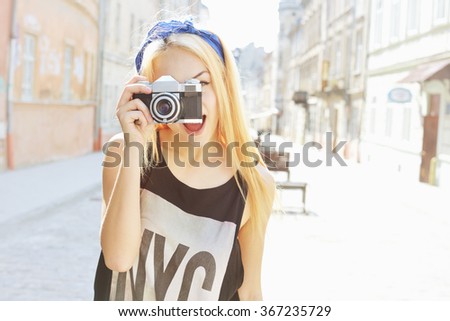 Outdoor summer lifestyle portrait of pretty woman having fun in city with camera. Travel photo of photographer. Making pictures, hipster style. Blonde girl looking at camera. Young woman taking photo