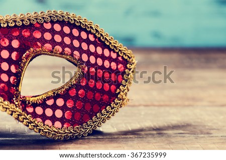 an elegant red and golden carnival mask on a rustic wooden surface