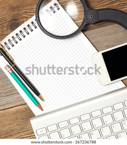 notebook, computer keyboard, pen, smartphone and magnifying glass on old wooden table surface. Still-life with objects for finding and recording information in web