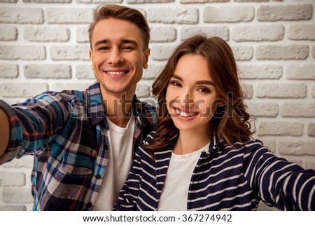 Happy young couple makes selfie, dressed in stylish clothes on brick wall background. Close-up