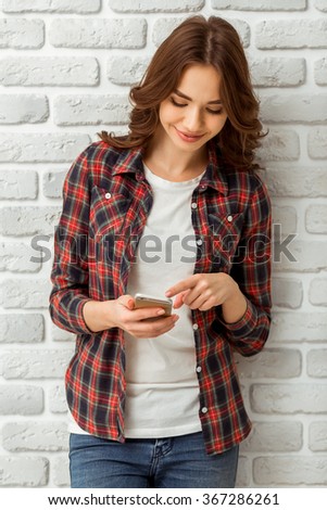 Attractive young woman using the phone with a smile, standing on the brick wall background