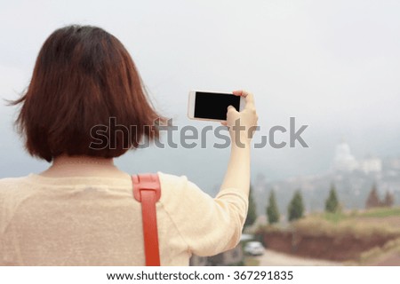 Back view of woman taking photograph with smart phone camera at the mountain