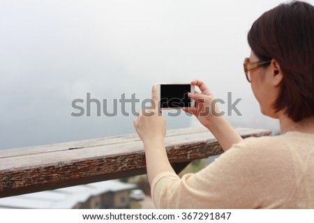 Back view of woman taking photograph with smart phone camera at the mountain