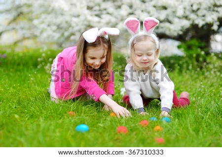 Two adorable little sisters hunting for easter egg in blooming spring garden on Easter day
