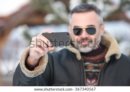 Handsome man take a picture of himself with a smartphone over winter background, focus on phone