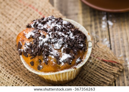 One tasty sweet dessert muffin baking with chocolate crumb and powder sugar on top in paper case standing on brown sackcloth fattening nutrition food closeup on wooden baklground, horizontal picture
