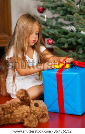 Cute Child with teddy bear toy finding her Christmas present in the morning still in her sleepwear and unwrapping it