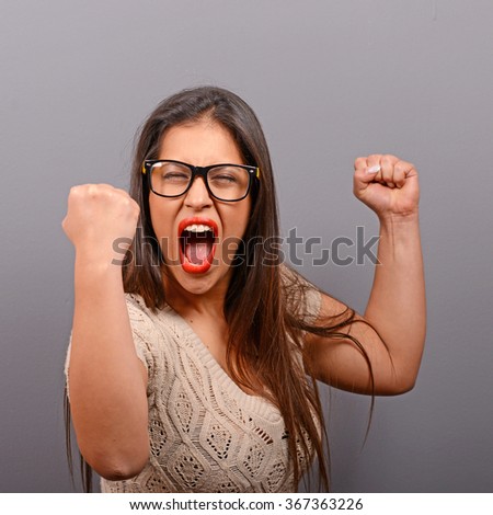 Portrait of happy woman exults pumping fists ecstatic celebrates success against gray background