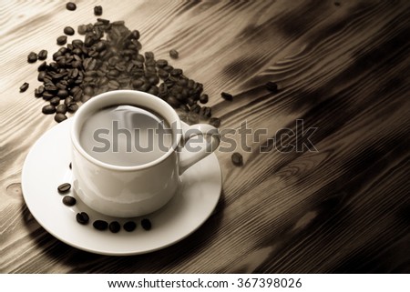 Coffee beans and coffee in white cup on wooden table. Selective focus. Toned.