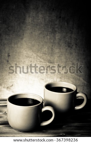 Coffee in cup on wooden table opposite a defocused burlap background. Toned.