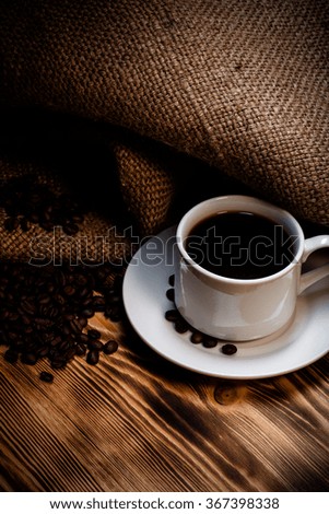 Coffee beans and coffee in white cup on wooden table with burlap. Toned.