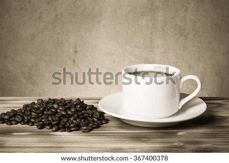 Coffee beans and coffee in white cup on wooden table opposite a defocused burlap background. Toned.