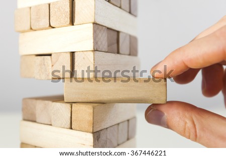 The tower from  wooden blocks and man's hand take one block Royalty-Free Stock Photo #367446221