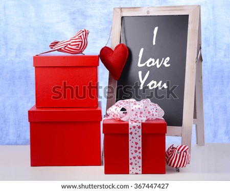Valentine chalkboard with red gifts and bird ornaments on white wood table and blue background, with I love You sample text. 