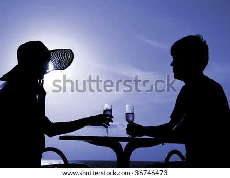 Pair silhouette sit at a table and hold goblet with wine on a moon night