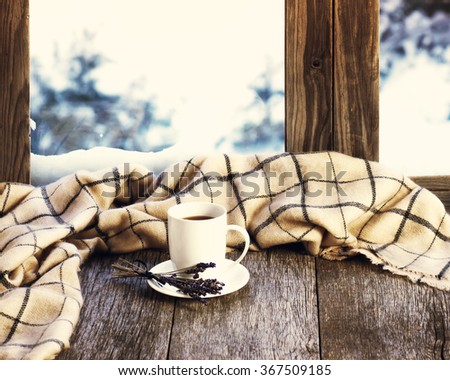 White cup of coffee or tea, lavender flowers and woolen plaid located on stylized wooden window sill. Winter concept of comfort and relaxation. Photo with retro filter effect.