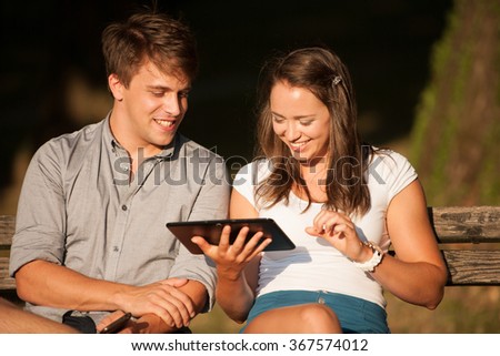 Young couple having fun on a bench in park while socializing over web