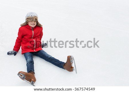 positive happy boy being silly and sitting on ice enjoying winter vacation at outdoor ice skating rink 