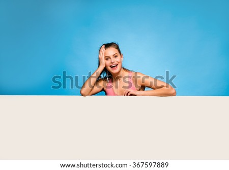 young pretty woman with pink sport shirt and headsets having an empty panel in front on blue background