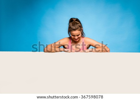 young pretty woman with pink sport shirt and headsets having an empty panel in front on blue background