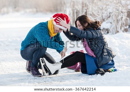 Happy couple having fun ice skating on rink outdoors. Man helping to wear ice skates to his girlfriend. Winter sport and leisure concept. Love and fun in wintertime.