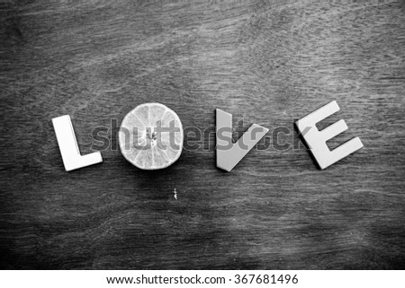 word love made up of colorful wooden letters with slice of orange instead of letter O on a wooden board. February 14, Valentine's Day. Black and white.