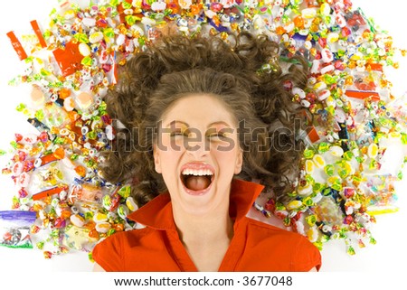 Young, beautiful woman lying on floor among candys with closed eyes. Laughing, front view. White background
