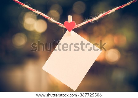 Blank white paper and red clip paper heart hanging on the clothesline with bokeh nature background.Designer concept.vintage or retro tone.