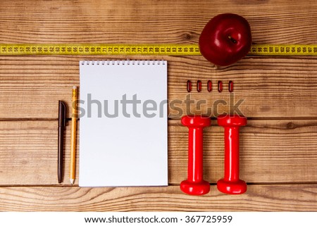Apple, tape measure and notepad with dumbbells lying on a wooden table