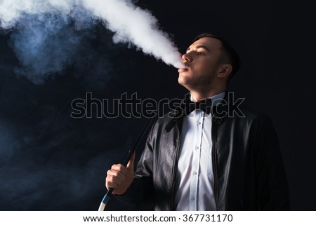 Young, handsome man smoking a hookah. It produces smoke from his mouth. Business style clothing. The pleasure of smoking.