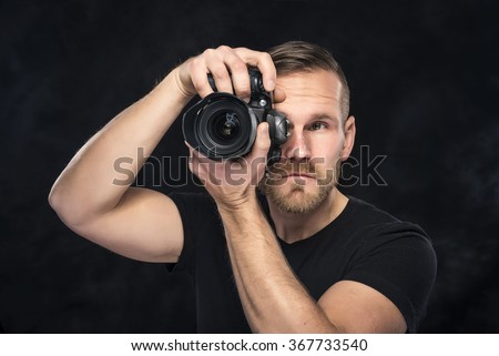 Photographer man with camera on darck background. Focus on camera.