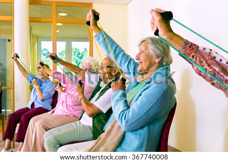 Group of older women seated in chairs using stretching bands for physical fitness class Royalty-Free Stock Photo #367740008