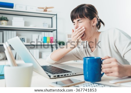 Tired sleepy woman yawning, working at office desk and holding a cup of coffee, overwork and sleep deprivation concept Royalty-Free Stock Photo #367741853