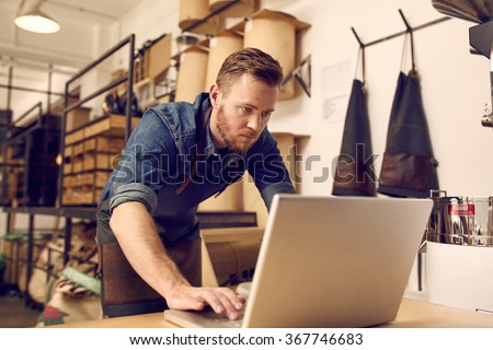 Serious young business owner using laptop in his workshop Royalty-Free Stock Photo #367746683
