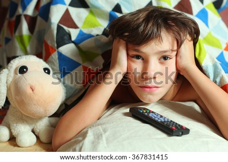 preteen handsome boy lay in bed with sheep toy and remote tv control watching favorite cartoon program