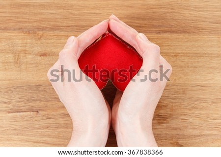 Heart symbol in hands. Concept of health, protection and love. Woman holding heart in her hands. On wooden background