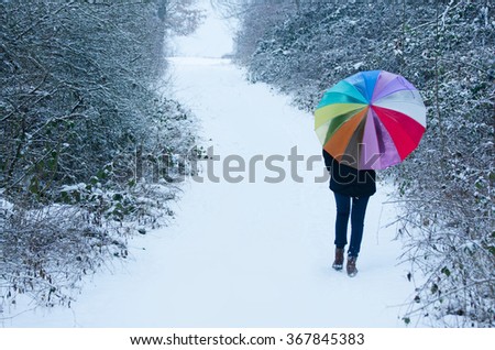 Umbrella with rainbow colors holding by young girl surrounded by winter nature 