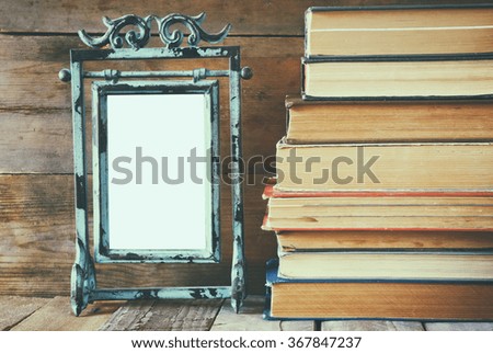 stack of old books next to vintage blank frame wooden table. vintage filtered image
