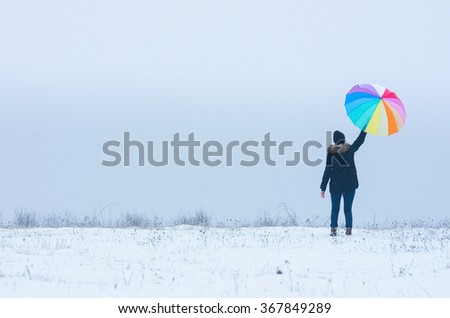 Alone girl in winter nature hold in hand beautiful umbrella with rainbow colors