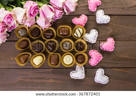 Assorted chocolated with pink roses on wood table.