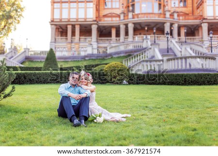 Pretty couple hugging and flirting in an urban park sit on lawn a wreath on his head, holding flowers in their hands summer