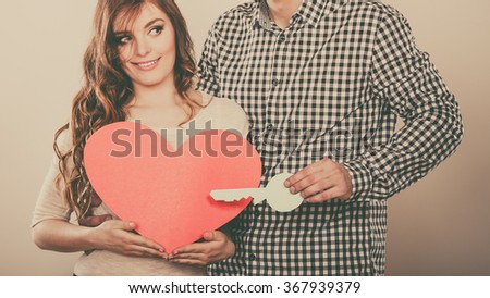 Smiling young couple holding paper key to heart sign love symbol. Loving husband and wife dreaming about new home. Instagram filtered.