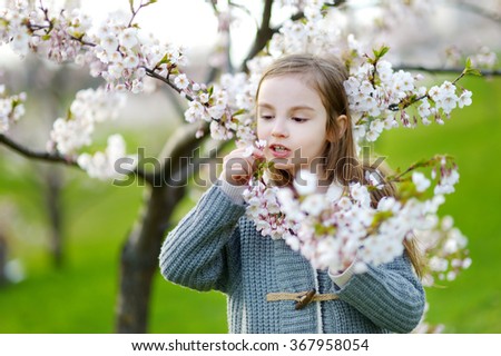 Adorable little girl in blooming cherry garden on beautiful spring day